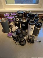 Overview of all travel mugs spread on surface with some lids removed and placed alongside mugs.