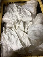 Top view of a yellow plastic crate filled with white cotton gloves, some loose and some in transparent plastic bags.