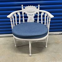 Front view of the white settee chair displaying the blue round cushion and intricate carved backrest.