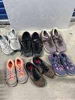Lot of 8 pairs of women’s sneakers in various colors and styles, visible signs of use, grouped together on a gray concrete floor.