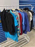 Lot of 9 assorted women's tops hanging on black metal rack in storage unit area, showing full variety of colors and patterns