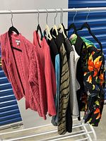 Wide angle of the 8 women's clothing items on hangers on a clothing rack, including knitted pink sweaters and patterned skirts or tops.