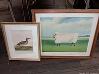 Framed lithographs of a duck and a 'Prize Ram' sheep on a floor with chairs in background