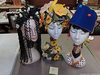 Group photo showing three artisan decorated foam wig stands with floral and ribbon details.