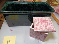 Photo showing the rectangular dark green glazed pottery planter alongside the square pink and white speckled lidded box on a table.