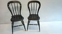 Two black lacquered chairs with spindle backs and floral stencil decor on backrests and legs, placed side by side against a white background.