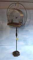 Full height view showing brass bird cage hanging from circular hoop atop turned stand and ornate base