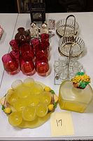 Photo showing full lot including Lemoncello set of frosted yellow glasses and decanter with decorative stopper, cranberry glass cordial glasses, crystal serving bowls and tray, salt and pepper shakers, small art glass vase, and decorative cranberry bottle.