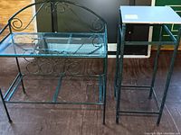 Metal glass topped wine rack table and matching green metal tile top stand shown side-by-side on the floor.