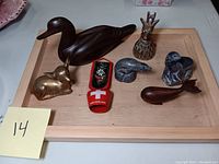 Full lot on wooden tray including brass reindeer bell, brass fox figurine, wooden duck, wooden sea animals, and two Swiss textile souvenirs.