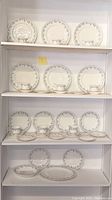 Full shelf view of the entire dinnerware set with plates, teacups, and saucers arranged on shelving showing pattern and quantity.