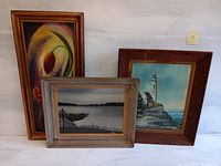 Four framed original paintings including a colorful abstract still life, a seascape with lighthouse, a small boat seascape, and one additional painting.