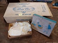Box labeled Bridal Chest by DES-L Industries, partially opened showing white lace baby clothing and shoes inside a box.