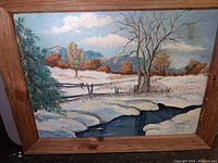 Frontal image of the signed oil on board painting showing the snowy creek, trees, rustic fence, and partly cloudy sky in winter setting, framed in wood.