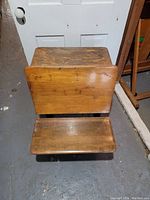 Front view of the antique child's school desk showing the wooden seat and desktop with the fold-down lid.