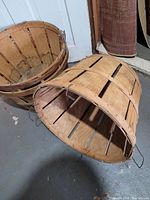 Three wooden apple baskets with wire handles, showing rustic wood slats and metal bands, placed on concrete floor.