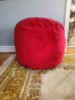 Photo of a large red cylindrical beanbag chair on carpeted floor with wall in background.