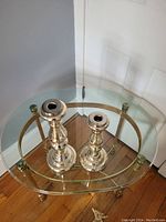 Pair of glass candlesticks on glass and brass table, showing both tall and short candlesticks with metallic finish.