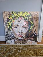 Front view of the large square canvas print showing a stylized woman's face made of newspaper clippings and paint.