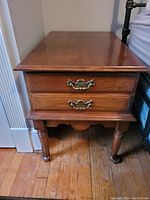 Front view of wood end table showing two dovetail joined drawers with brass handles, turned legs and scalloped apron.