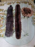Photo showing two long fur collars and one round fur hat on a glass table with floral carpet.
