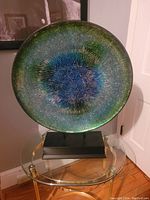Front view of the large circular mosaic decor piece showing blue, green, and black mosaic pattern on glass-like surface mounted on a stand.