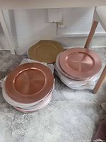 Stacks of gold and rose gold plate chargers placed on the floor, showing the metallic finish and circular design with recessed centers.