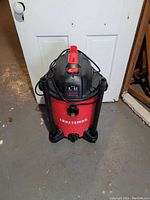 Front and top view of red Craftsman shop vac with hose holders and power cord wrapped on top, placed on floor in front of a white door.