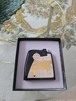 Photo of the vintage desk lighter featuring a world map design in black and gold, placed inside a black box with a light purple interior lining.