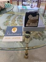 Vintage The Statesman desk lighter displayed on glass table next to its original box and instruction pamphlet.