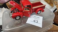 Photo of 1940 Ford red pick-up truck model showing open hood and left door with visible detailed engine and interior. Model is placed on a translucent plastic surface with seller's lot number card visible.