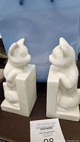 Front view of the pair of white porcelain cat bookends showing the two cats sitting facing each other with their paws over the base.