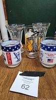 Photo showing five glasses including two Apollo 11 souvenir glasses with patriotic and moon landing graphics, one McDonald's Hamburgler glass with character artwork, and two clear glasses with vintage Mickey and Minnie Mouse graphics.