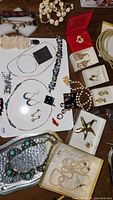 Mixed jewelry items on a table, including turquoise earrings, various necklaces, pearl necklace, starfish brooch, and earrings in boxes.
