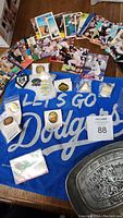 Overview of lot showing spread of baseball cards, Dodgers hand towel laid flat with visible text, assorted pins mostly in packaging, and pewter dish partially visible.