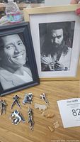Photo of framed celebrity photos of The Rock and Jason Momoa with Marvel X-Men pins and miniature marble horse figurines on table.