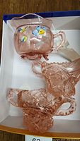 Photo of the pink cut glass sugar bowl and matching creamer alongside the footed, hand-painted creamer showing details of cut patterns and floral decoration.