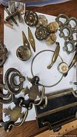 Photo showing various vintage brass drawer pulls of assorted styles including round knobs, ornate handles, and plates laid out on a table.