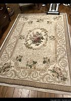 Photo showing a 5x7 area rug with floral and scroll patterns in beige and pink tones on wooden floor.