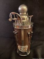 Front view showing the golf ball shaker top and golf club shaped bar tools arranged in the golf bag case with attached golf tees.