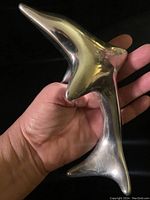Hand holding the metal dolphin sculpture to show size and scale.