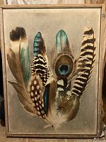 Full view of the framed oil painting depicting feathers on canvas.