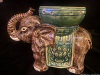 Side view of vintage ceramic elephant planter showing detailed textured brown body with green planter saddle and embossed lotus design.