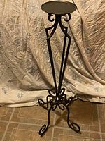 Full view of the wrought iron candle holder showing its height and scroll base design against a fabric backdrop.