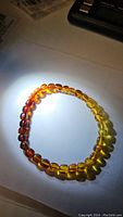 Bracelet displayed on white surface with light highlighting the gradient color from deep reddish-brown to yellow amber beads.