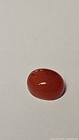 Oval cabochon polished mandarin orange carnelian gemstone showing color and glow under different lighting.