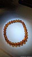 Amber bracelet laid out in an oval shape under direct light, showing translucent warm amber beads with internal variations.