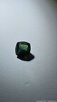 Close-up photo of a natural sapphire gemstone showing cushion cut shape, blue-green color, and faceted surface.