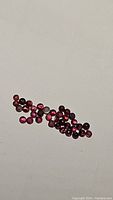 Top-down view of multiple small round calibrated rhodolite garnet gemstones scattered on a light surface.