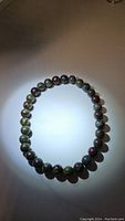 Photo of Dragon's Blood Jasper bead stretchy bracelet showing rounded polished beads with green and red natural color patterns on elastic string.